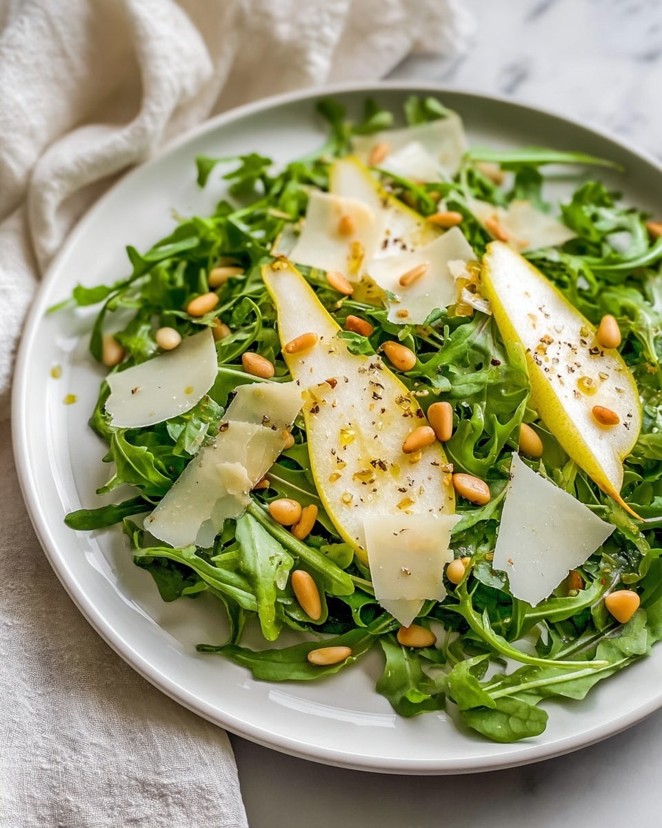 A white plate holds a fresh arugula salad as the base layer, with bright green leaves spread evenly. On top, there are thin slices of pear with a yellow skin and juicy pale flesh, placed in a scattered pattern. Small pine nuts are sprinkled across the salad, adding light brown accents. Thin, irregular shavings of pale white cheese are spread over the salad. Everything is lightly coated with a drizzle of olive oil and sprinkled with cracked black pepper. The plate is set on a white marbled surface with a blurred light cloth in the background. photo taken with an iphone --ar 4:5 --v 7