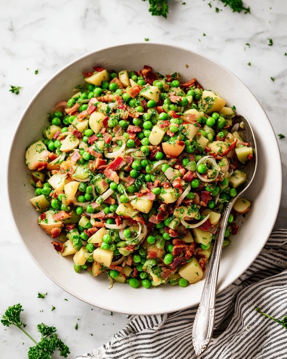 A white bowl filled with a colorful mix of layers including bright green peas, small light yellow potato cubes, thin light brown onion rings, and small diced reddish-brown bacon pieces, all mixed evenly and garnished with small green parsley bits, with a metal spoon resting on the side of the bowl. The bowl is placed on a white marbled surface with some scattered green parsley leaves around and a striped cloth napkin partially visible at the bottom right. Photo taken with an iphone --ar 4:5 --v 7
