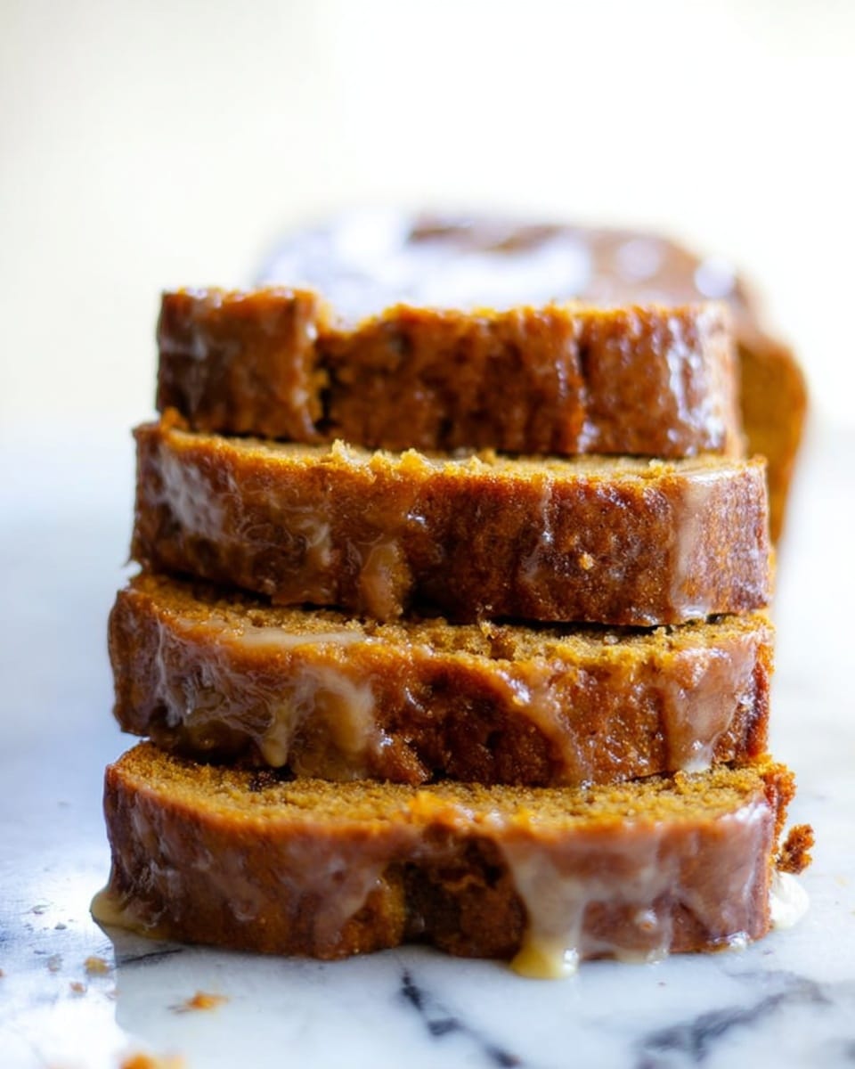 The image shows a stack of four slices of moist, golden-brown bread with a rich, slightly shiny glaze that drips down the sides. The bread layers appear dense with some darker spots indicating ingredients like fruit or nuts inside. The top of the stack is flat and crumbly, with the glaze adding a slight sheen to the surface. The background features a white marbled texture on which the bread rests, making the warm tones of the bread stand out clearly. Photo taken with an iphone --ar 4:5 --v 7