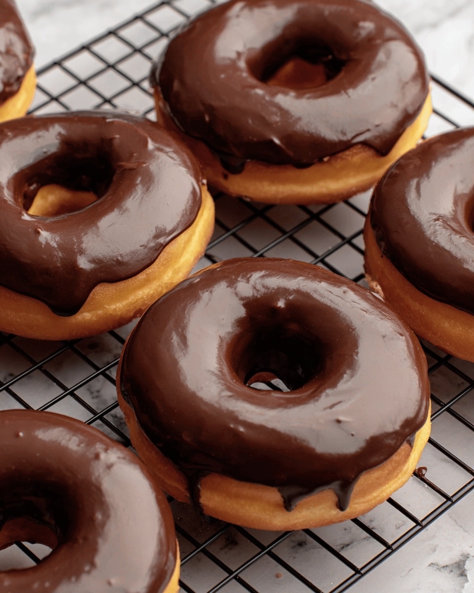 The image shows six donuts arranged on a black cooling rack placed on a white marbled surface. Each donut has one layer of light golden-brown dough with a smooth, shiny chocolate glaze layer on top. The glaze covers the top half of each donut evenly, with slight drips on the sides, showing a rich, dark brown color and glossy texture. The donuts have a soft and fluffy texture visible on the dough edges, contrasting with the smooth chocolate coating. photo taken with an iphone --ar 4:5 --v 7