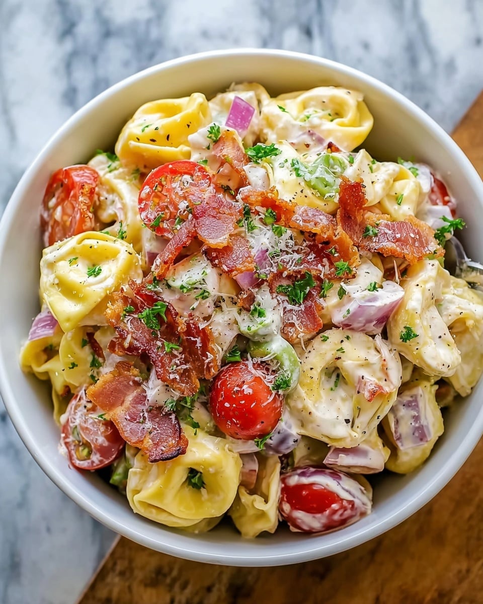A white bowl filled with a creamy tortellini pasta salad featuring three layers: the bottom layer is yellow tortellini with a smooth texture, mixed evenly with pieces of red onion and green olives. The middle layer has bright red cherry tomato halves and crispy bacon strips scattered throughout, adding color and crunch. The top layer is coated in white creamy dressing, sprinkled with freshly grated white cheese and small green parsley leaves on a white marbled surface. Photo taken with an iphone --ar 4:5 --v 7
