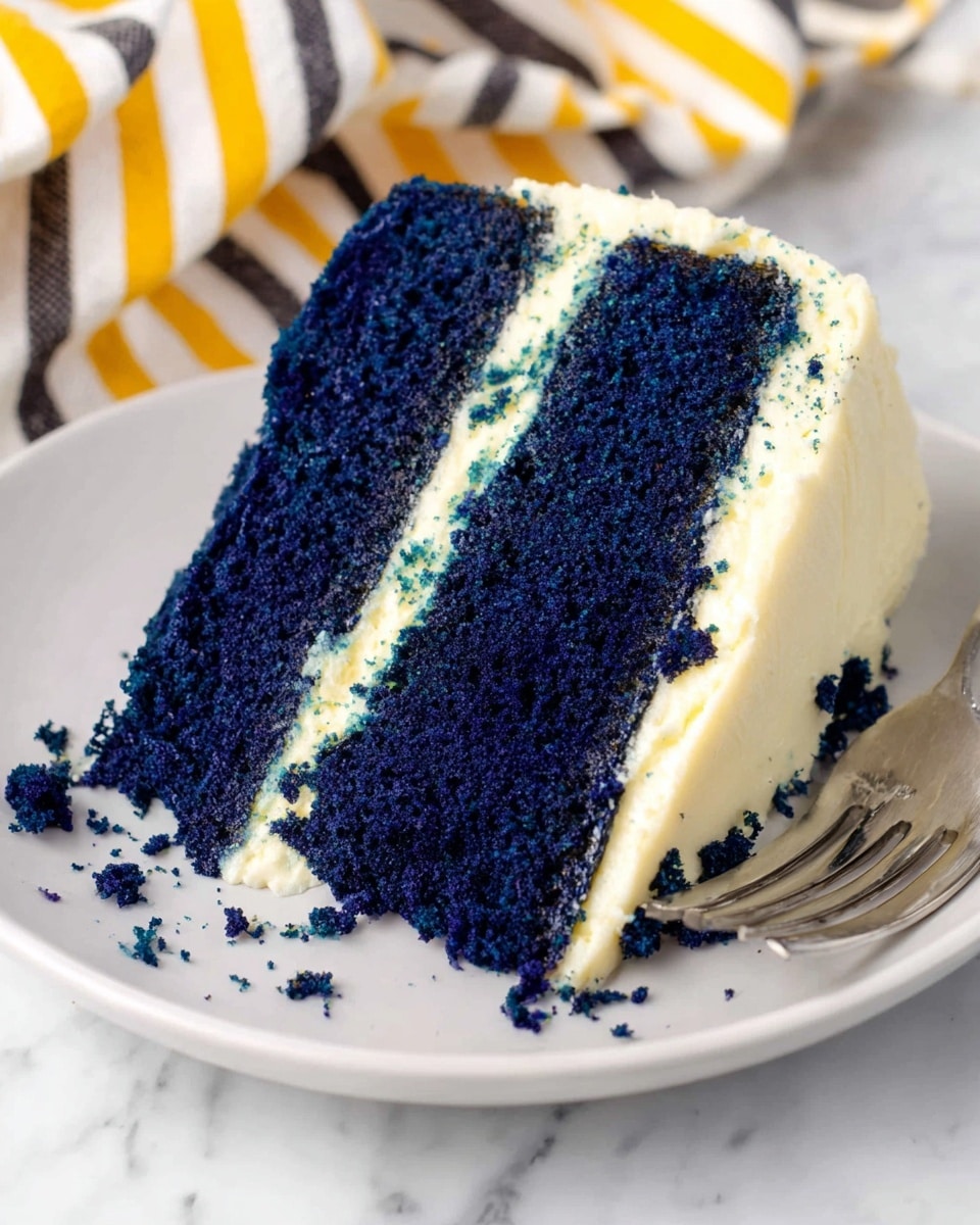 A slice of three-layer dark blue cake with white cream frosting between each layer and on the sides, sitting on a white plate. Each blue cake layer looks soft and crumbly, with thick, smooth white frosting in between. There are cake crumbs scattered on the plate and a small piece cut off with a silver fork resting nearby. The background is a white marbled surface with a striped cloth in yellow, black, and white colors partially visible in the upper part of the image. Photo taken with an iphone --ar 4:5 --v 7