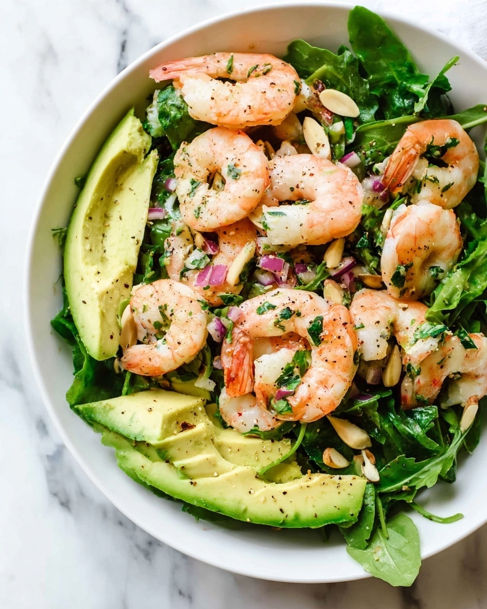 A fresh shrimp salad in a white bowl on a white marbled surface, showing multiple layers: at the bottom, bright green arugula leaves create a leafy base with some sliced almonds scattered in; on top of that, large pieces of sliced avocado with pale green creamy texture are spread around; the top layer features neatly arranged cooked shrimp, pink and white with a slight sheen, sprinkled with chopped herbs and small bits of finely chopped red onion; the salad has a light sprinkle of black pepper adding small dark specks over the ingredients. photo taken with an iphone --ar 4:5 --v 7