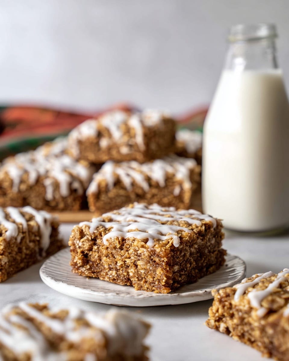 The image shows several square oat bars with a chewy texture and a golden brown color, drizzled with thin white icing on top. One oat bar is centered on a small white plate with a slightly scalloped edge, showing its dense oat and spice inside layers with a moist look. Around the plate, other oat bars are placed directly on a white marbled surface, some overlapping each other. In the background, there is a glass bottle filled with off-white milk, slightly out of focus. The overall composition highlights the oat bars’ rough texture and the contrast of the smooth white icing against their warm brown tones. photo taken with an iphone --ar 4:5 --v 7