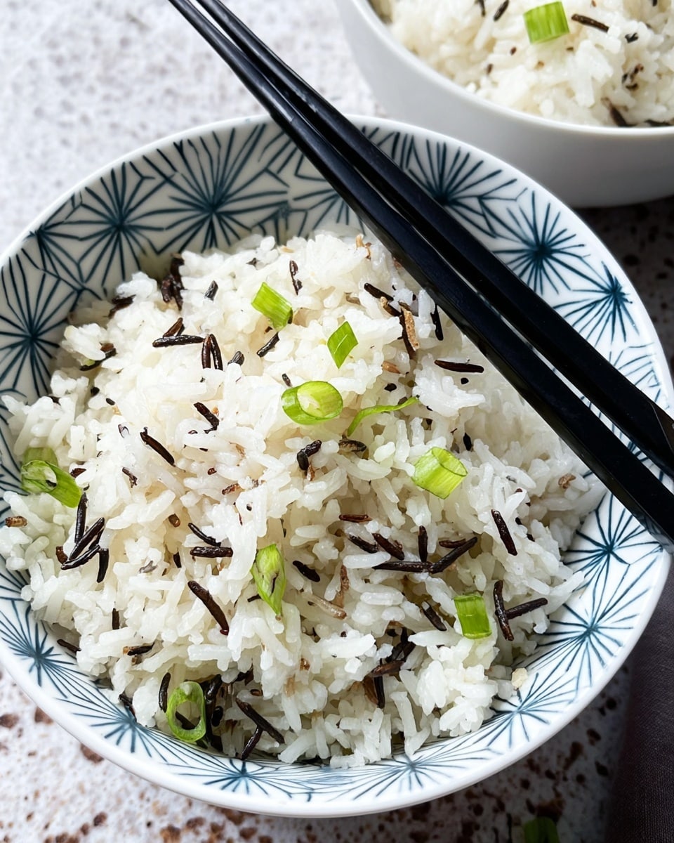 A close-up of a single bowl filled with fluffy white rice mixed with a few strands of dark wild rice, topped with small pieces of chopped green onions scattered over the surface. The bowl is white with a blue geometric star-like pattern on the inside, and two black chopsticks rest diagonally across the right side of the bowl. The bowl sits on a white marbled textured surface with a glimpse of another bowl of white rice in the top right corner. photo taken with an iphone --ar 4:5 --v 7