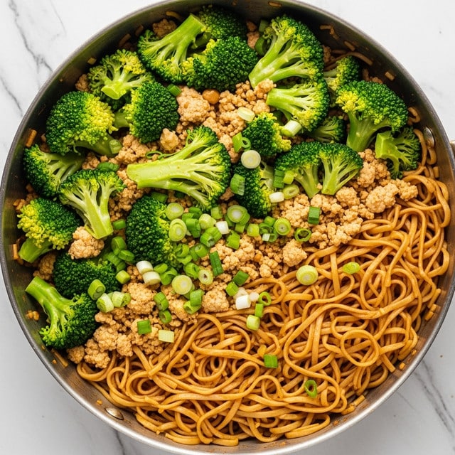 A pan filled with a mixed dish showing three main layers: at the bottom, a layer of light brown rice noodles with a soft and slightly glossy texture; on top of that, chunky bright green broccoli florets that look fresh and crisp; scattered throughout are small bits of light beige ground tofu or similar protein, adding a crumbly texture; finely chopped green onions sprinkled over everything add a fresh green color and texture contrast. The dish is inside a metal pan placed on a white marbled texture. Photo taken with an iphone --ar 4:5 --v 7